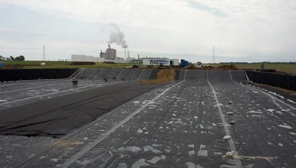 A shallow basin covered in a black liner. People are working on a portion of the basin in the background. On the ground above the basin is a semi with the JC Ramsdell logo on it.