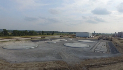 A shallow man-made basin with circular bases in it. A dirt lot surrounds it, with a trail showing where vehicles drive down into the basin.