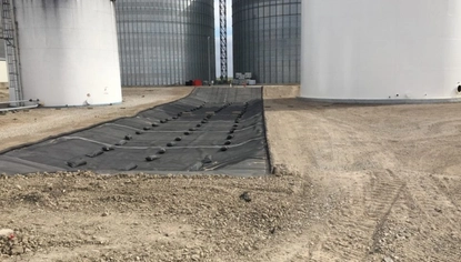 Two white tanks with two gray grain bins. In the middle is a long, skinny stretch of black lining on the ground, held down with small rectangular objects.