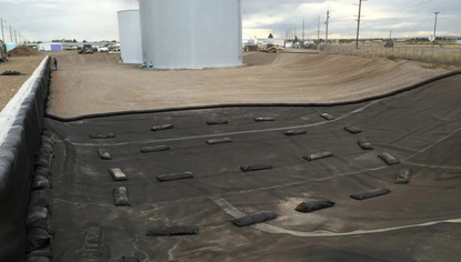 A large, shallow basin with two large white container tanks at the far end. At the front is a black liner that covers the ground and wall that fences in part of the basin. It's held down by rectangular black objects.