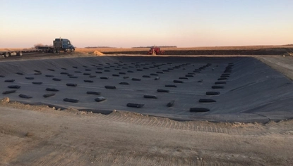 A short basin covered in a black liner, held down by black rectangular objects. To the left of the basin sits a dark blue semi-truck.