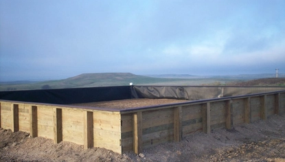A fenced-off area made of wood. The interior of the fence and the ground inside it are lined with a large black covering, with dirt contained in it.